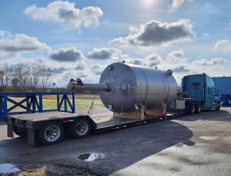 The back of an oversized freight truck with a large shipment in the open truckbed. A blue sky and white clouds sit in the background.