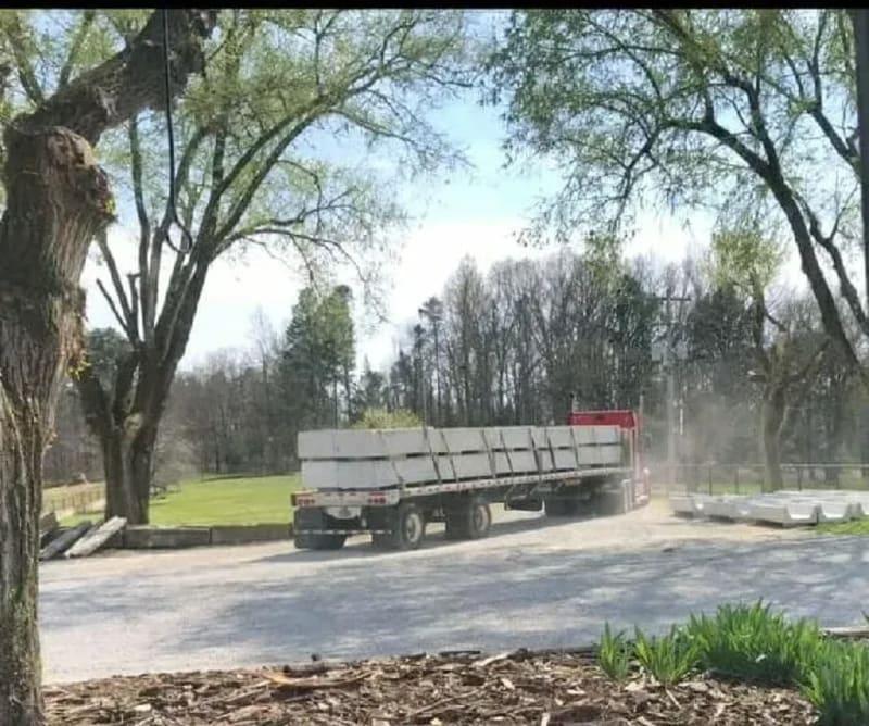 A red truck drives off with concrete cattle bunks loaded onto the truck bed.