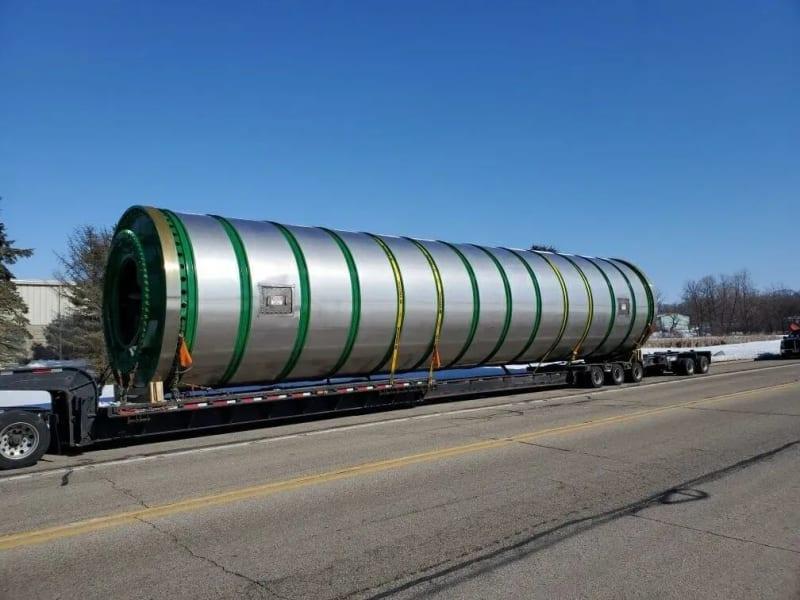 A massive cylindrical dryer strapped on a truck bed.