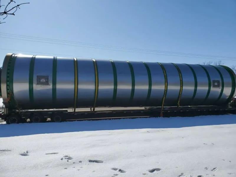 Another angle of a massive cylindrical dryer strapped on a truck bed. 