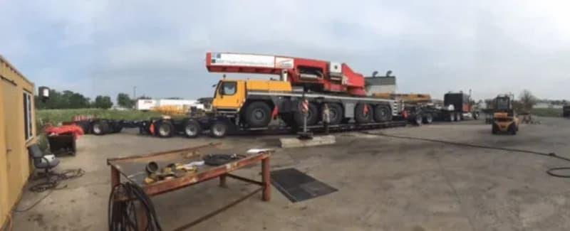 A large yellow truck carrying red equipment needed for the dam project.
