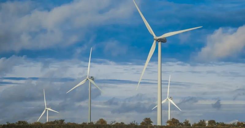 Four white wind turbines with a blue sky and clouds in the background.