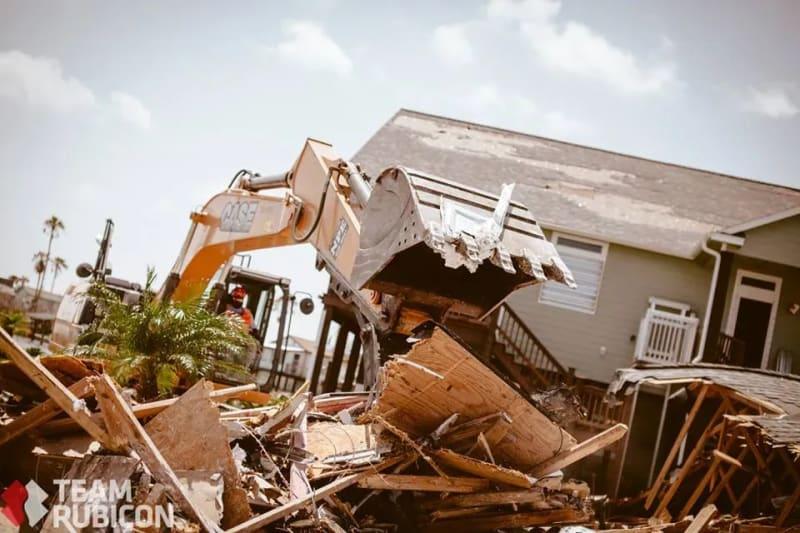 A construction vehicle makes its way through hurricane wreckage of a residence.
