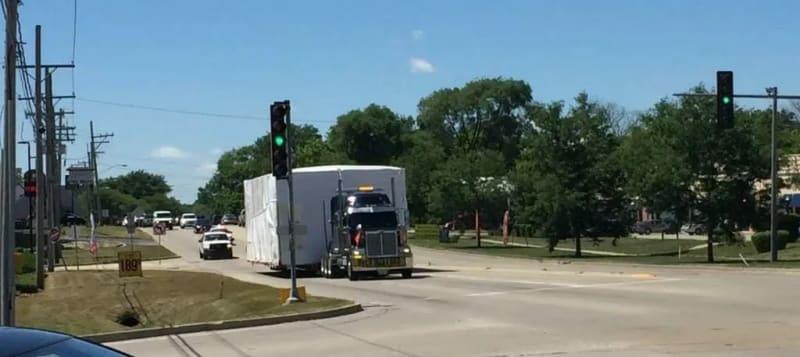 A truck driving into an intersection with a large prefabricated building on its bed.
