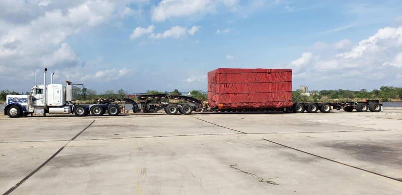 A 22-wheel truck carrying equipment covered in a red tarp.
