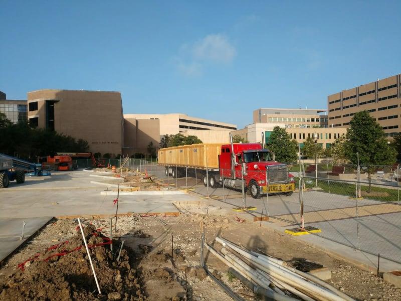A red truck carrying large wooden crates sits in front of a brown commercial building.