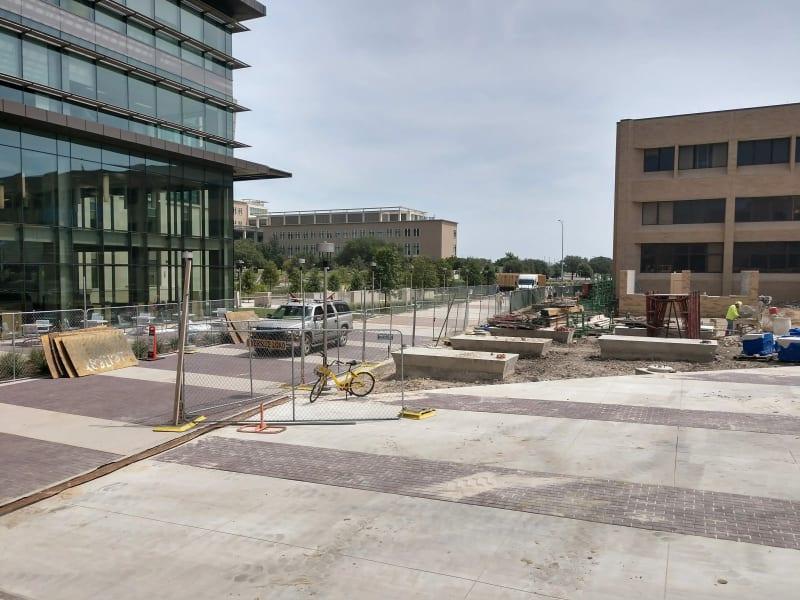 A job site with fencing, construction materials, and a small truck outside a commercial building.