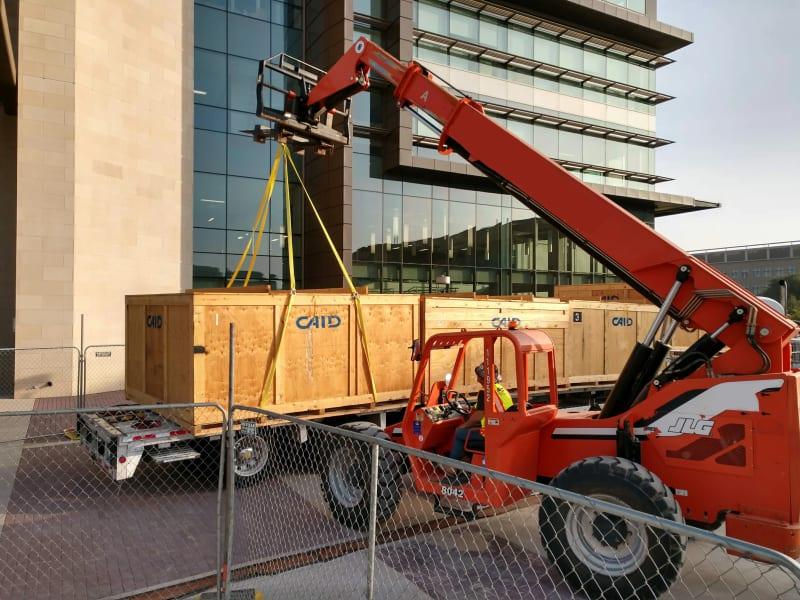 A red crane lifts a large wooden crate outside a commercial building.