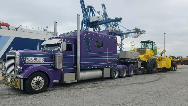 The side of a purple truck carrying a forklift in a parking lot.
