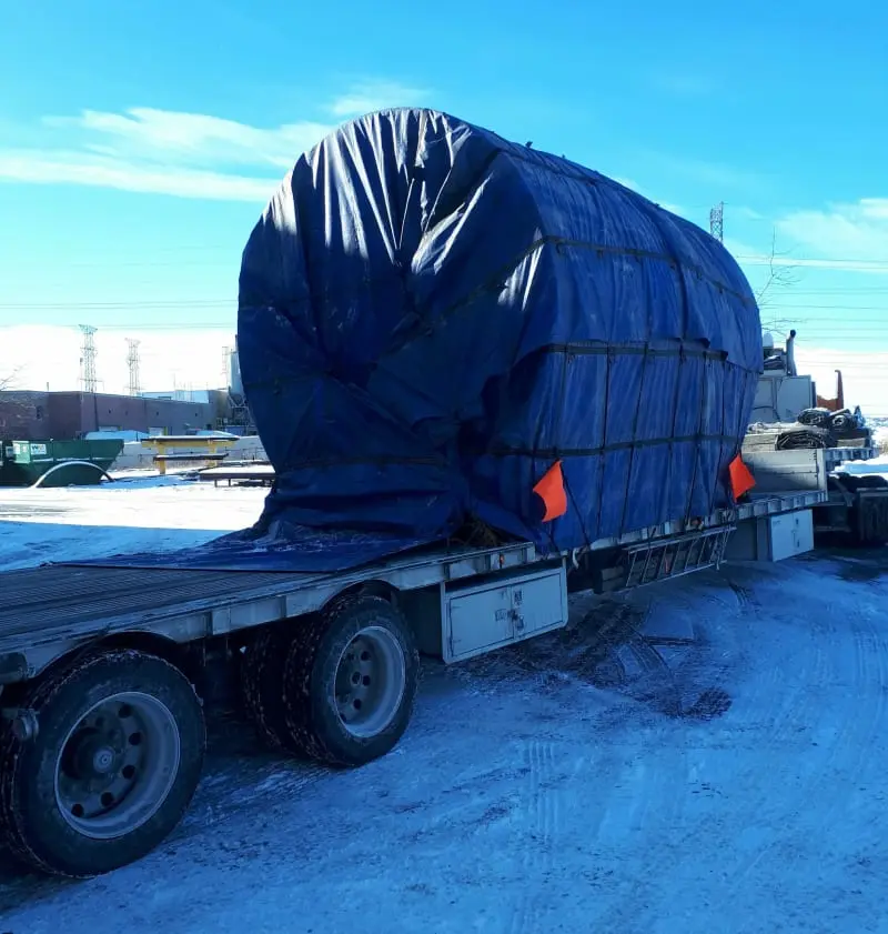 A thrust riding ring covered in a tarp and strapped to a truck bed.