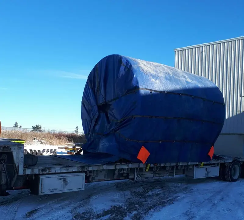 A side angle of a thrust riding ring covered in a tarp and strapped to a truck bed.
