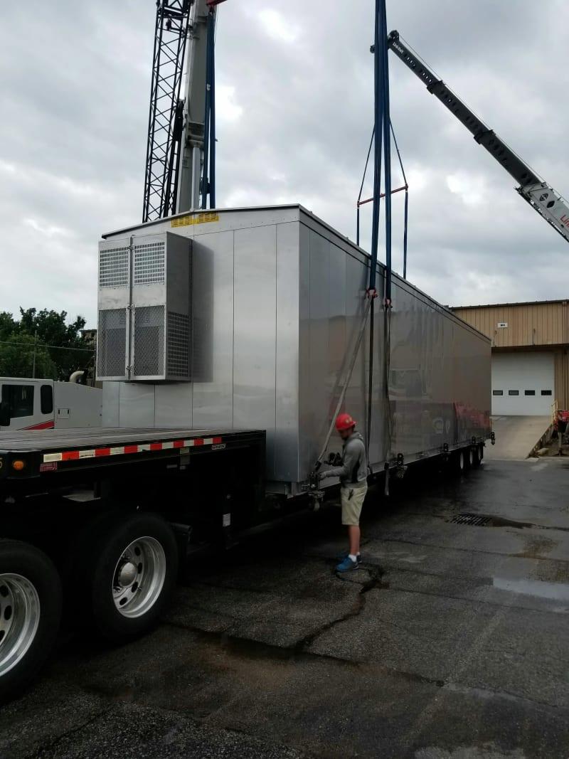 A relay house being loaded onto a truck bed with a crane.