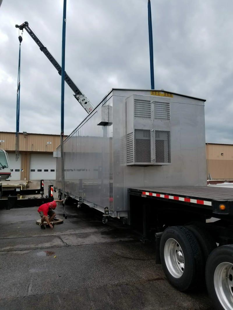 A relay house on the back of a truck being secured by a crew member.