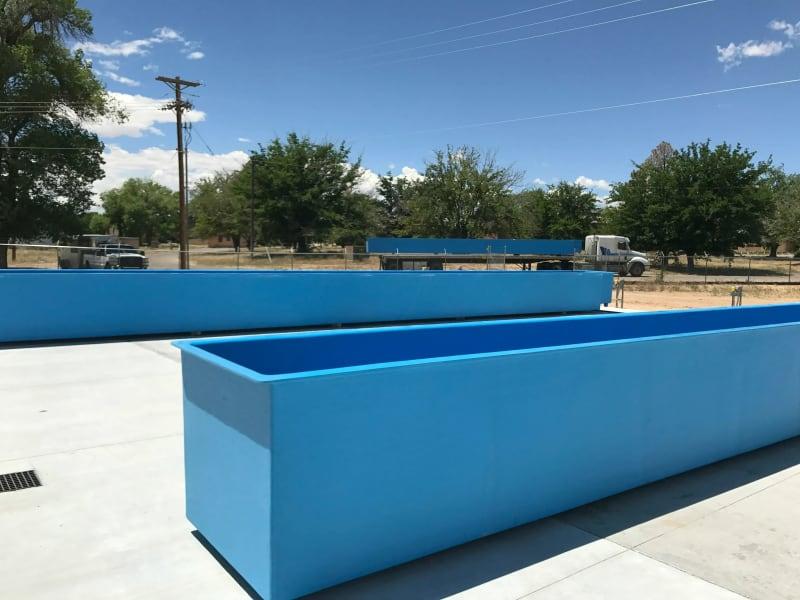 Two long blue fish farms sit side by side with the tops off.