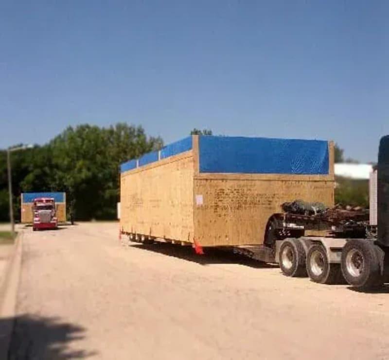Plant machinery in a wood crate covered in a blue tarp on a truck bed.