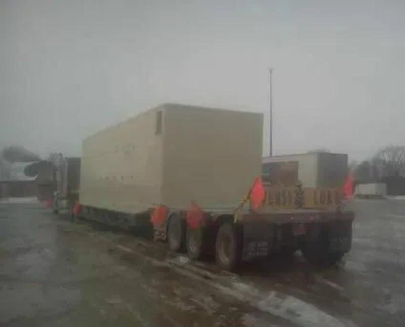 A large generator sits on the back of a truck on a rainy road.