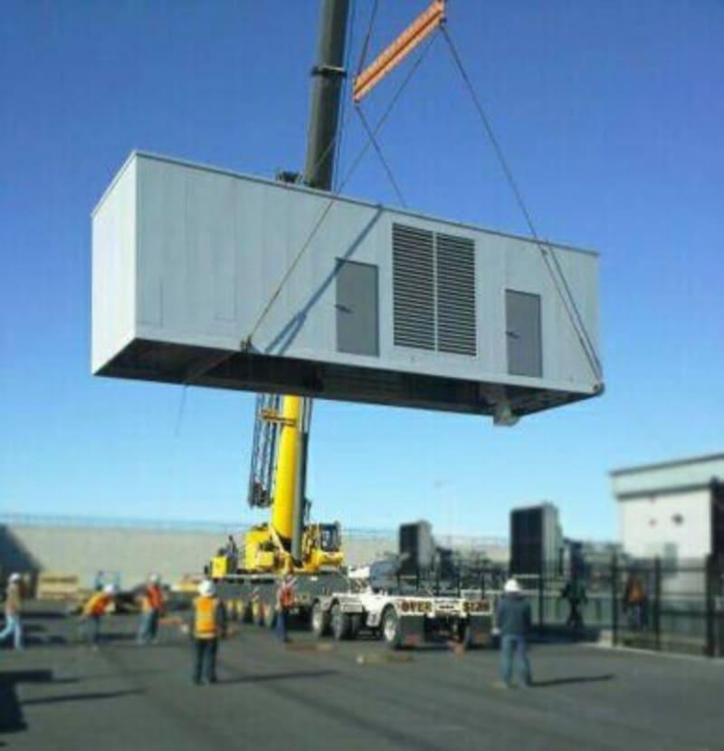 A generator being lifted by a crane to load onto a truck