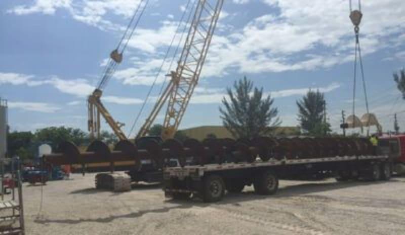 Drilling equipment loaded onto a truck bed with a crane in the background.