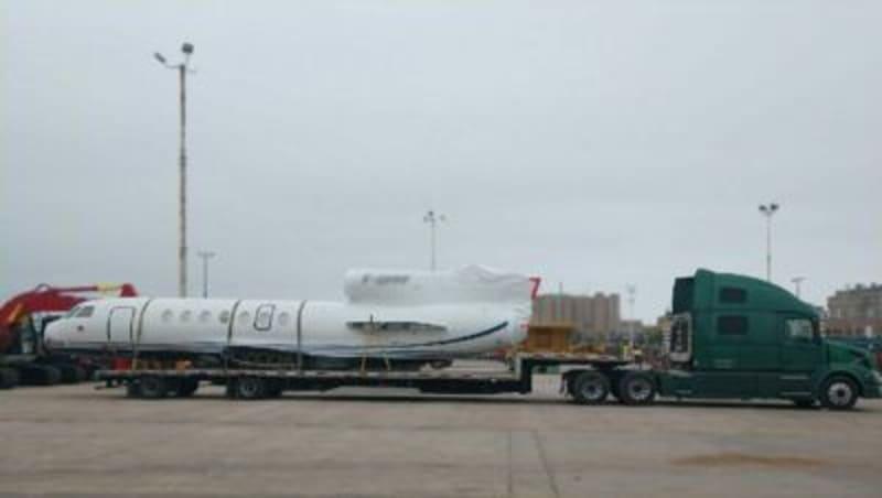 The front half of an airplane sits on the truck bed of a green truck.