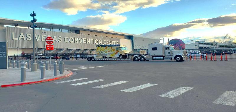 White truck carrying a colorful box truck on the back in front of the Las Vegas Conventional Center