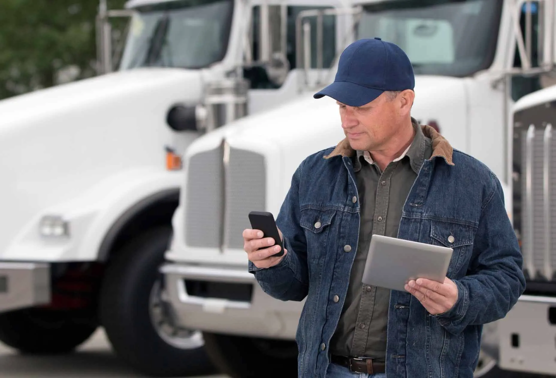 A ZMac carrier stands in front of his truck. He types on a cell phone with one hand while holding an iPad in the other.