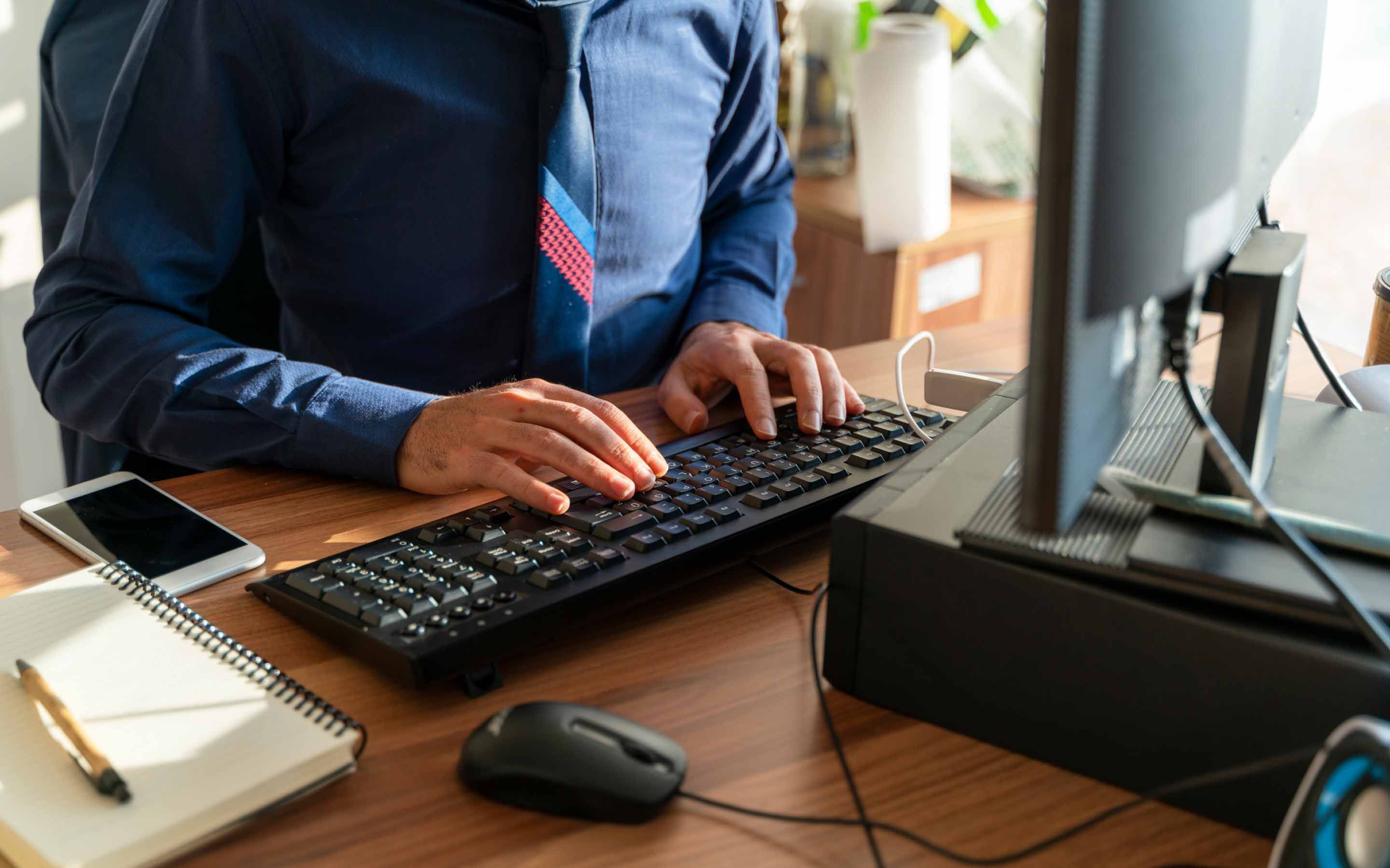 A man's hands type at a desktop keyboard.