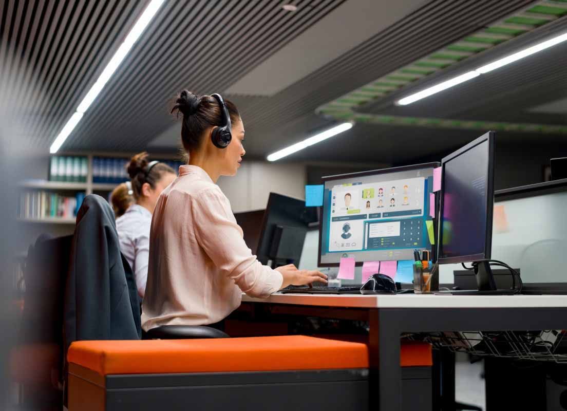 A customer service representative sits at a computer and types while wearing a headset.